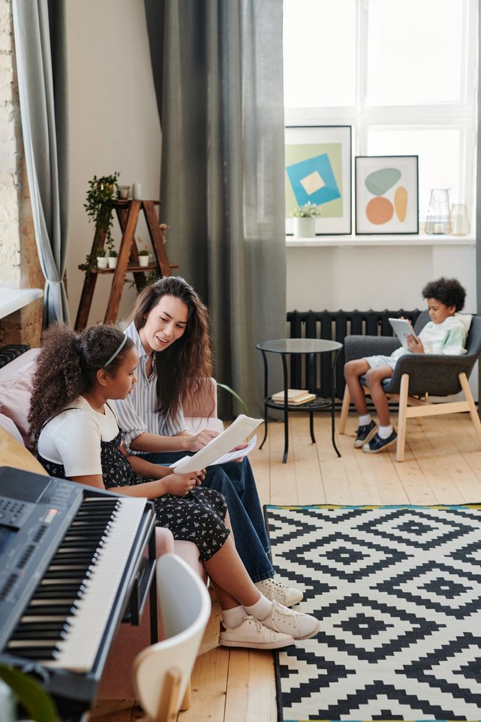 A woman tutors her children in a bright, modern living room with musical instruments.