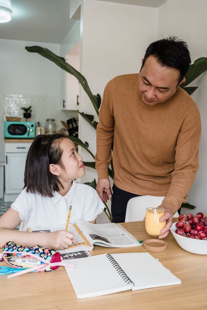 Father and daughter sharing a moment over homework in warm indoor setting.